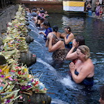 People performing a Balinese temple ritual, bathing under water spouts surrounded by traditional offerings
