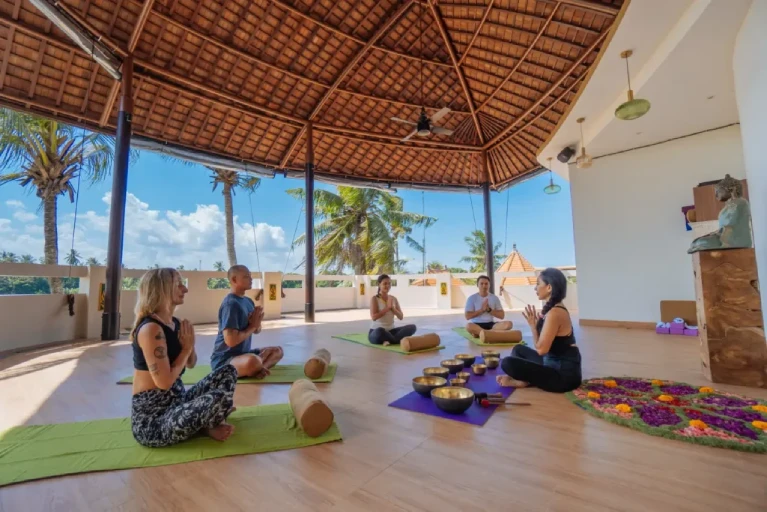 A group of people practicing meditation and sound healing in an open-air yoga studio