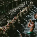 People performing a Balinese temple ritual, bathing under water spouts surrounded by traditional offerings