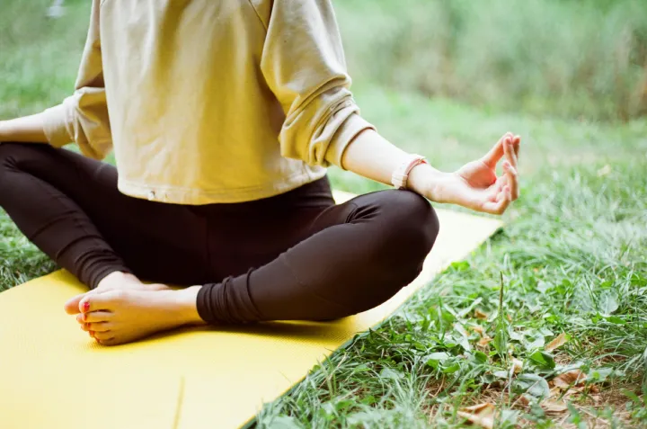 a girl doing a meditation pose on the top of grass with her mat